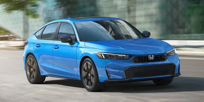 A blue Honda Civic hatchback with a black grille and black side mirrors driving on a blurred road