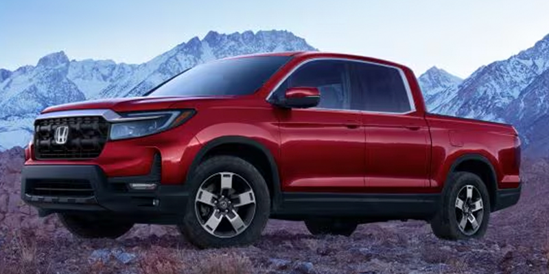 A shiny red Honda Ridgeline pickup truck parked on rocky terrain with snowy mountains in the background.
