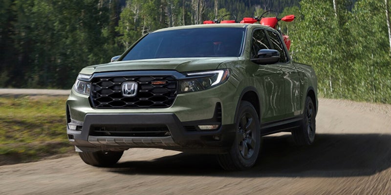 A green Honda Ridgeline TrailSport pickup truck with bikes loaded in the bed, driving on a dirt road.
