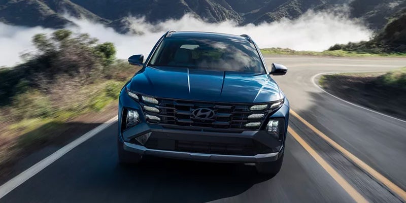Hyundai Tucson SUV driving on a winding mountain road with hazy clouds in the background.