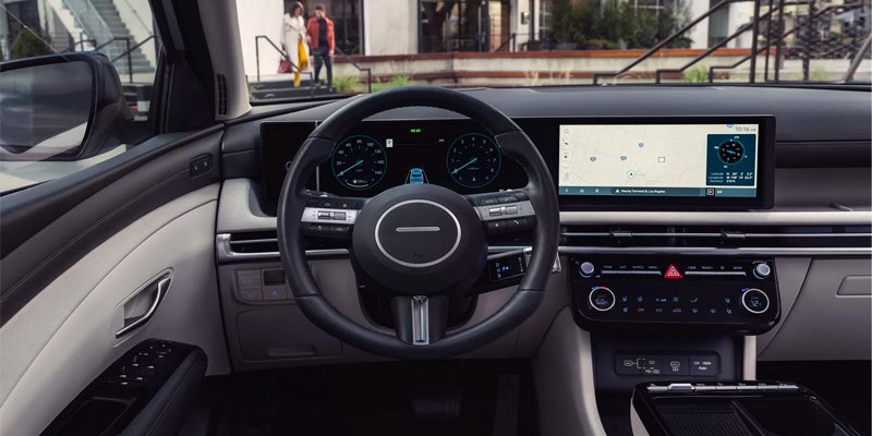 Interior view of a modern car's dashboard with a steering wheel, digital displays, and an outside view of people.