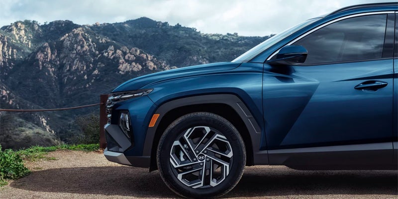Hyundai tucson with silver wheels parked on a dirt road, overlooking mountains.