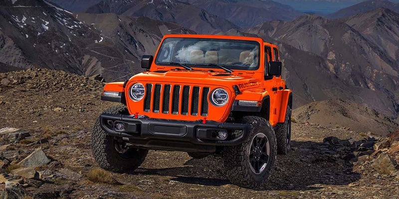 An orange Jeep Wrangler Rubicon SUV parked on a rocky mountainside