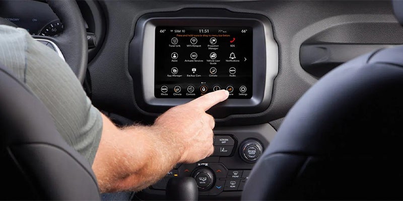 A man reaches from the driver's seat to touch the Store icon on a car black infotainment screen.