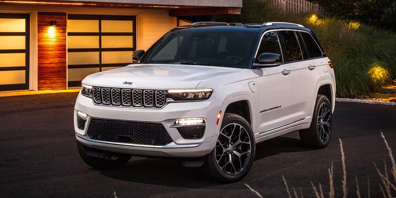 A white Jeep Grand Cherokee Laredo SUV with a black roof parked in front of a modern garage at dusk.