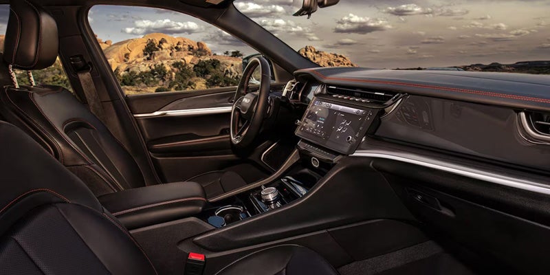 Interior view of a dark car with orange stitching, wide infotainment screen, and a desert landscape seen through the windows.