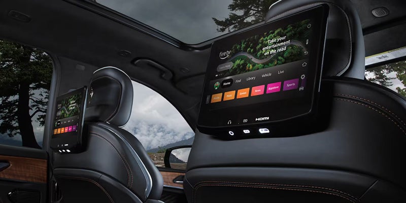Car interior showing two Fire TV tablets mounted to the back of black leather headrests for rear passenger entertainment.