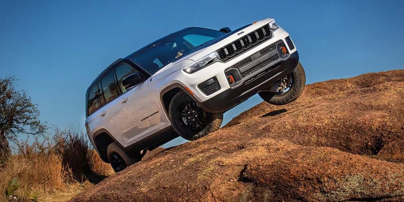 Grand Cherokee 4xe with a front wheel lifted, driving uphill on a rocky, uneven terrain.