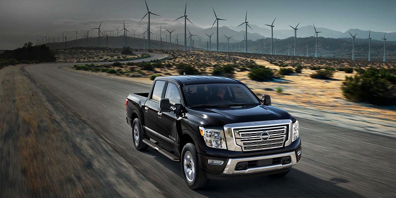 Black Nissan Titan pickup truck driving on a winding desert road lined with wind turbines.