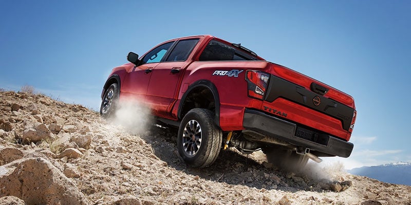 Red Nissan Titan Pro4X pickup truck driving up a rocky dirt hill, kicking up dust.