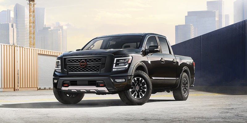 A black Nissan Titan Pro 4X pickup truck parked in an industrial area with shipping containers and a cityscape.