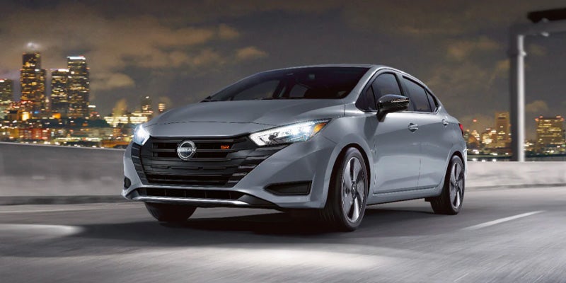 A gray Nissan Versa SR driving on a highway at night, with a distant city