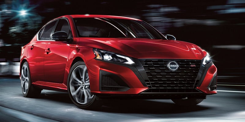 A glossy red Nissan Altima SR sedan blurred in motion against a dark background with bright lights.