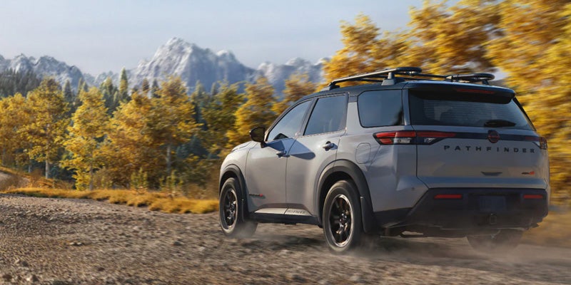 Nissan Pathfinder SUV driving on a dirt road, kicked-up dust visible, against an autumn mountain background.