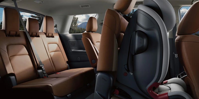 Nissan interior with a dark gray child safety seat in the foreground, brown leather seats, and a view of mountains.
