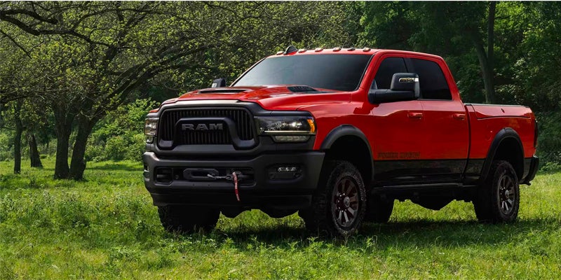 A red Ram Power Wagon pickup truck with black trim, parked angled on green grass with trees in the background.
