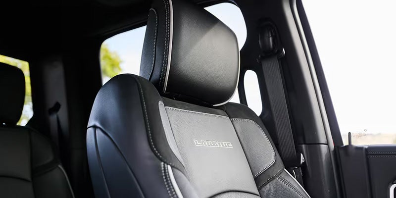 Close-up of a black leather car seat with LARAMIE embroidered in white, white stitching, and a seatbelt.