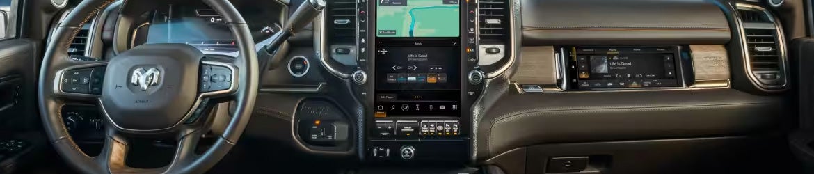 Close-up of a brown leather and wood car interior, showing steering wheel and large central touchscreens.