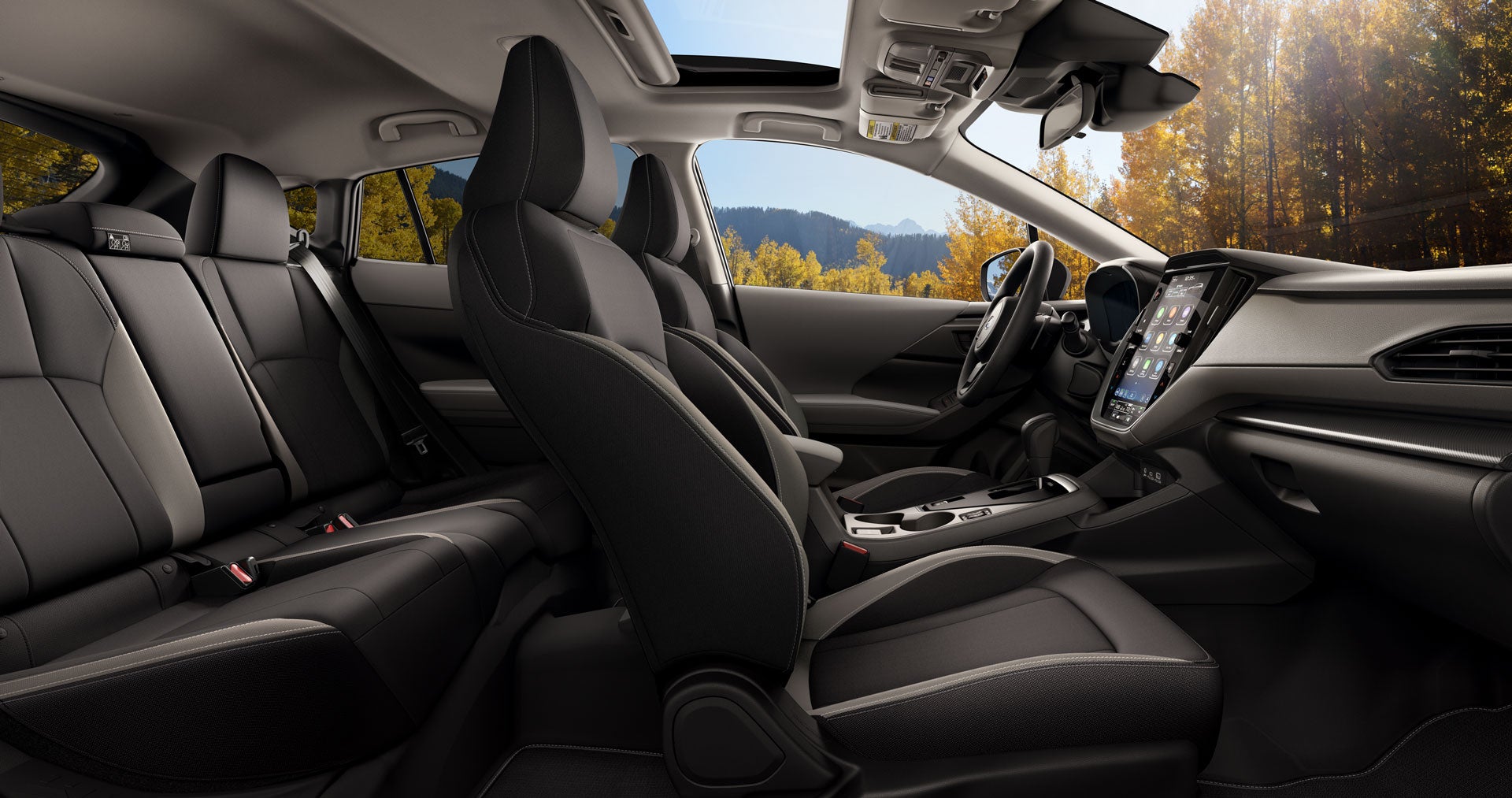 Interior of a modern car with black seats, a large touchscreen display, and a scenic autumn view through the windows.