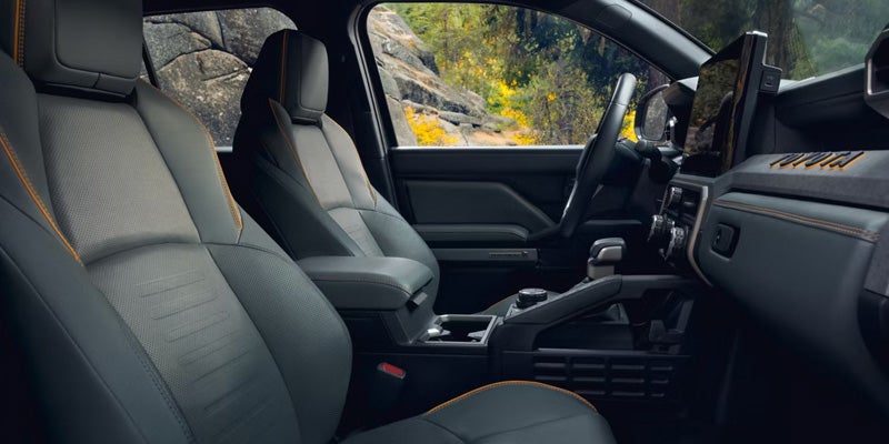 Interior of a car with dark grey and light grey seats trimmed with orange stitching, including a dashboard and steering wheel.