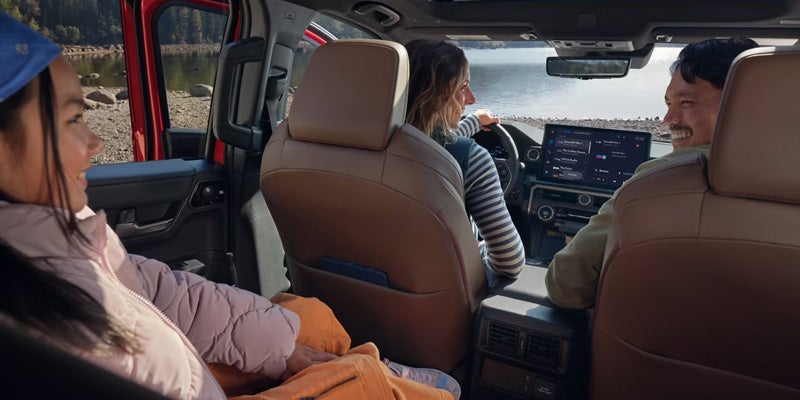 A family inside a vehicle by a lake, with two adults in front and a child in the back seat.