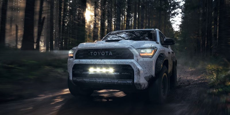 Toyota Tundra pickup truck driving through a rocky stream, splashing water, with a forest in the background.