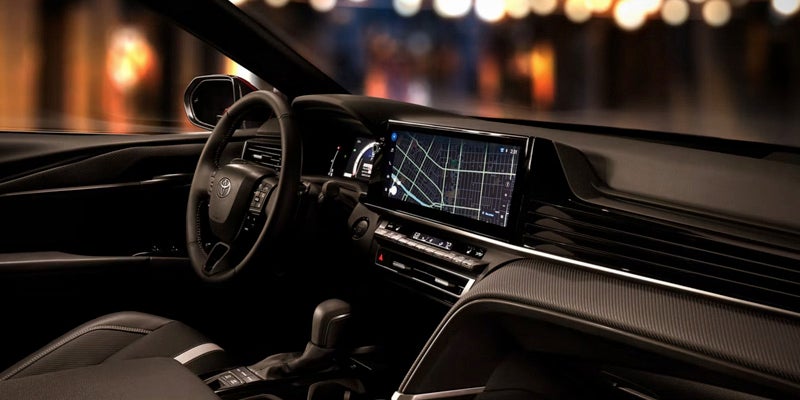 Interior of a car at night showing the dashboard, steering wheel, large infotainment screen with map, and gear shifter.