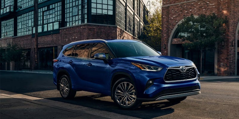 A dark blue Toyota Highlander parked on a street in front of brick buildings with large windows.