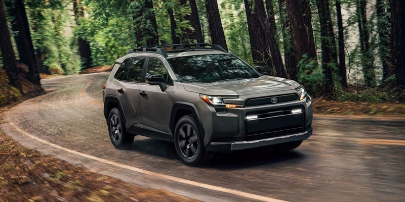 Taupe-colored Toyota RAV4 drives left on a winding, tree-lined road, blurring the forest in the background.