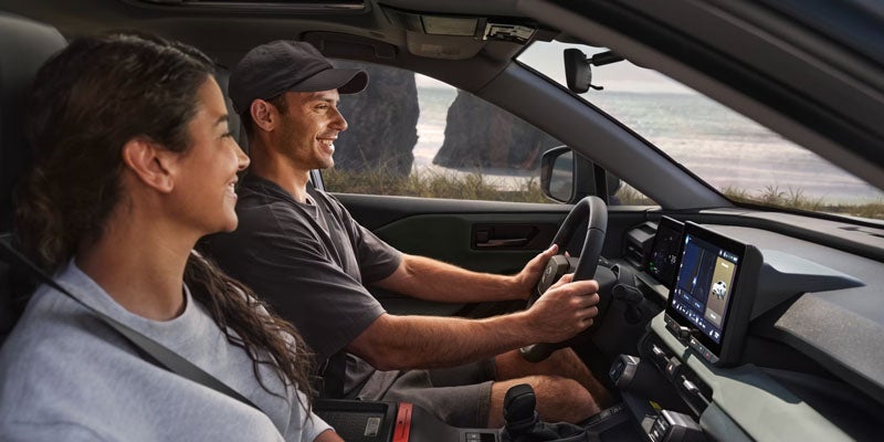 Man driving car with woman passenger, smiling and looking out at the ocean with cliffs in the background.