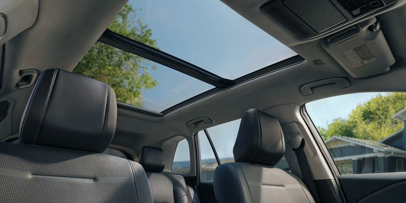 Panoramic sunroof extending over both rows of black leather seats in a car's interior, showing a blue sky and trees outside.