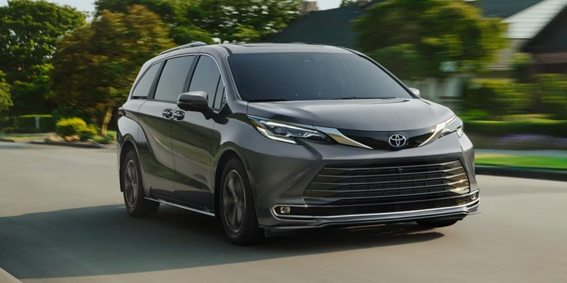 A dark gray 2023 Toyota Sienna minivan drives on a suburban street with motion blur.
