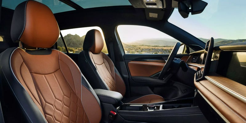 Car interior with brown and black leather seats, wood trim, and a desert landscape seen through the windows.