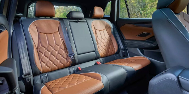 Rear interior of a car with three brown and black leather seats with hexagonal stitching patterns.