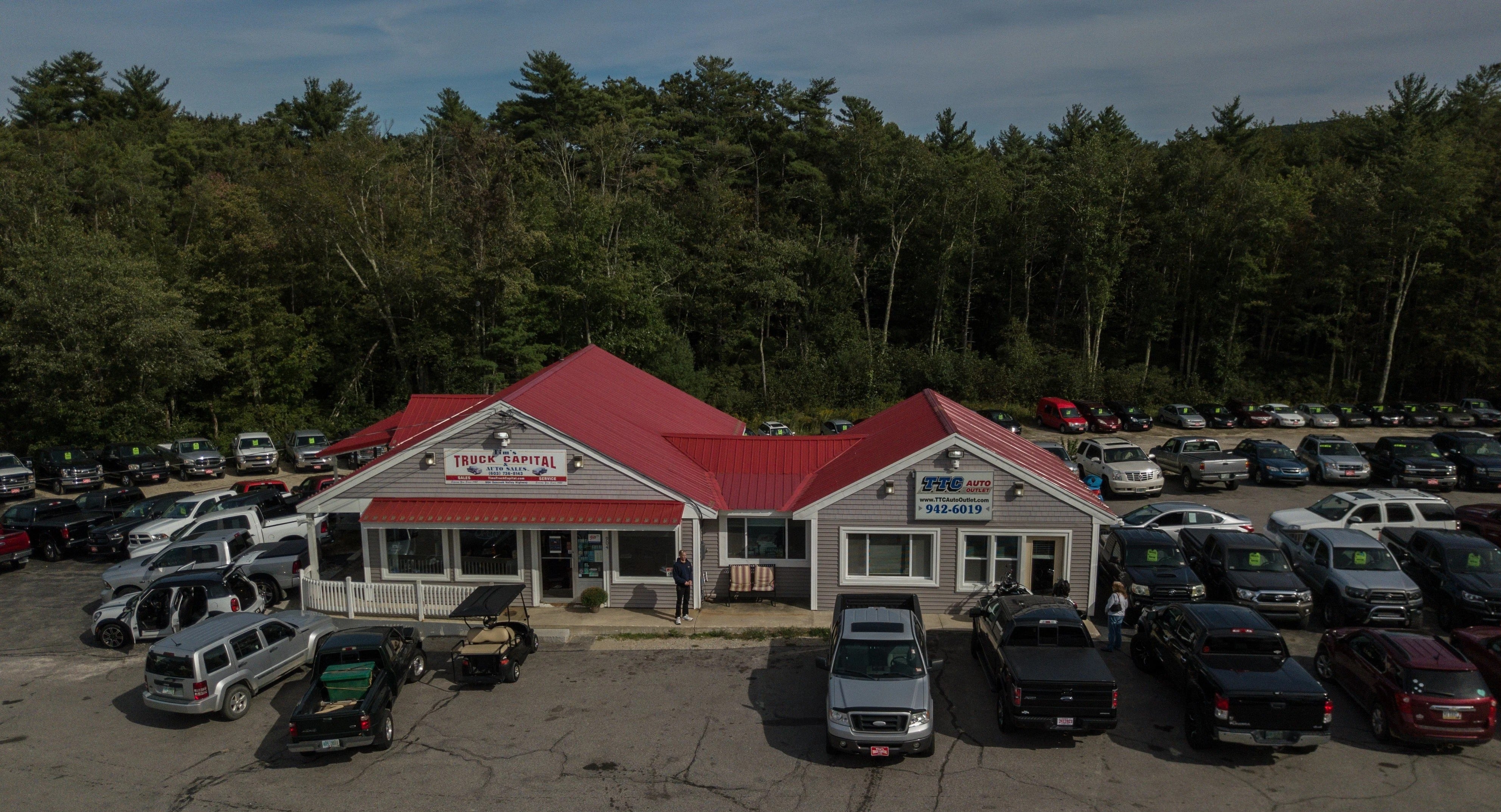 An aerial view of a gray building with a bright red roof, surrounded by cars on a large paved lot.
