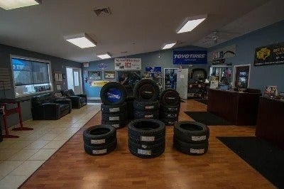 Interior view of a tire store showroom with stacks of tires on display and a small seating area.